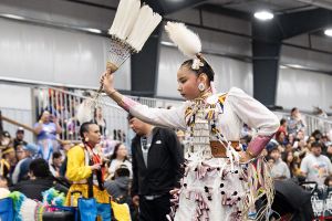 An Indigenous dancer in traditional clothing dances in front of an audience at the Manito Ahbee Festival.