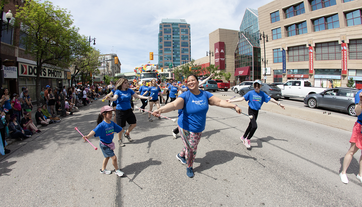 Manitoba Hydro employees walk in a Winnipeg’s Pride parade carrying a rainbow banner while a crowd cheers.