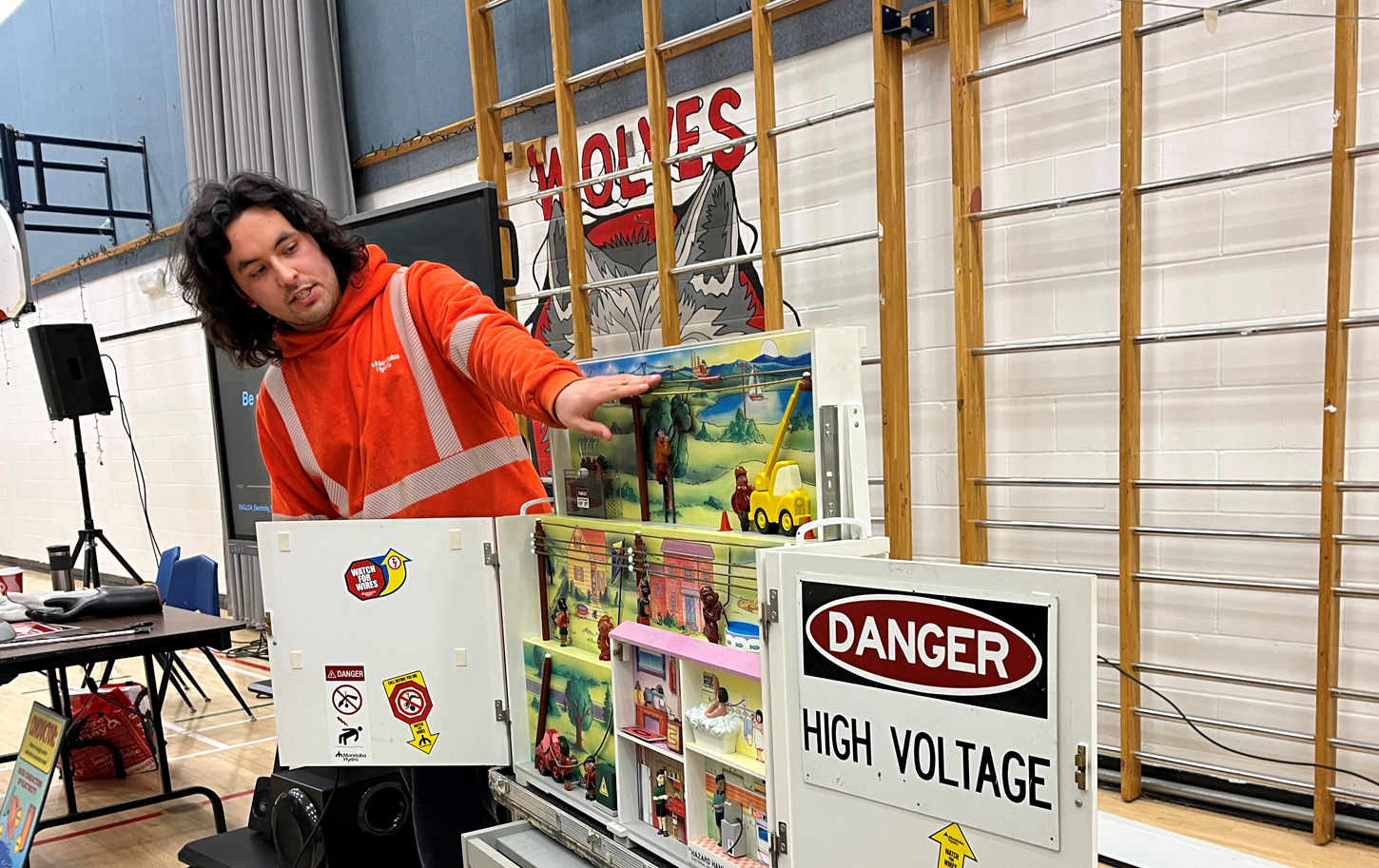 A Manitoba Hydro employee stands before a safety display in a school gymnasium to teach safety around natural gas and electric equipment to children.