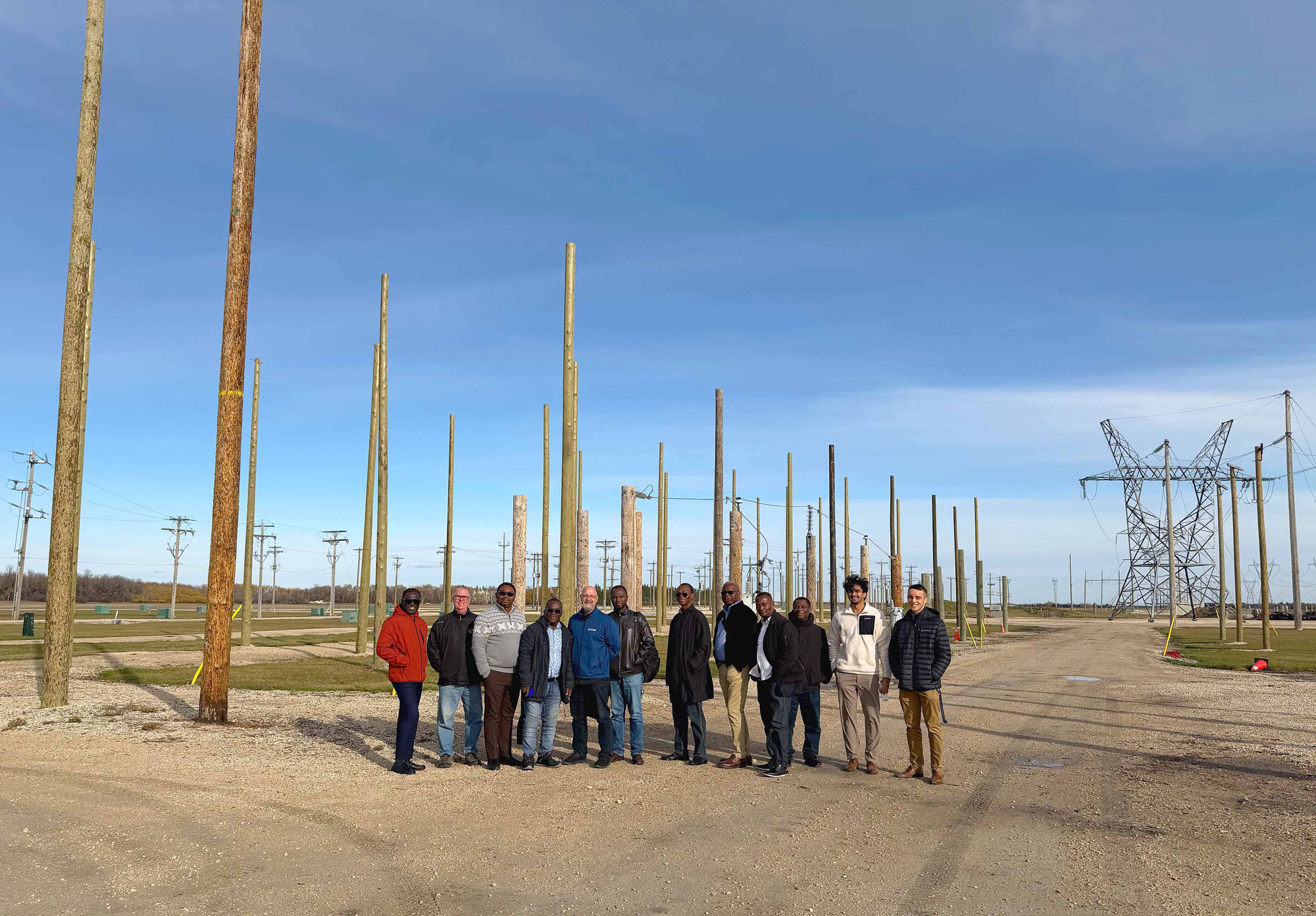 A group of men pose for a photo in front of hydro poles at a training facility.
